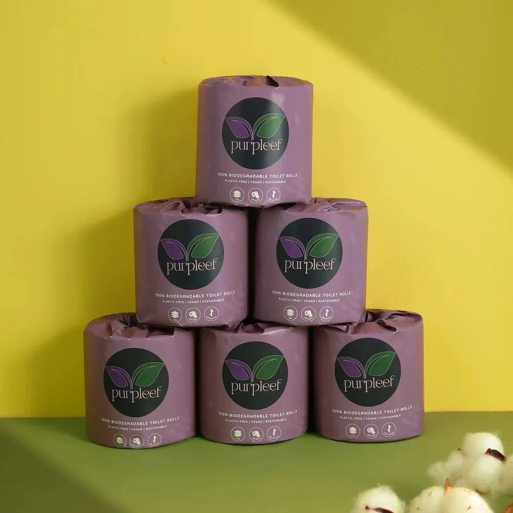 'Purpleef' toilet paper rolls stacked on a green surface with a yellow background