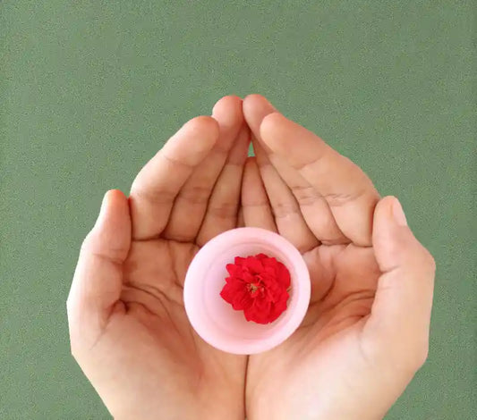 hands holding a pink menstrual cup with a flower inside on a green background