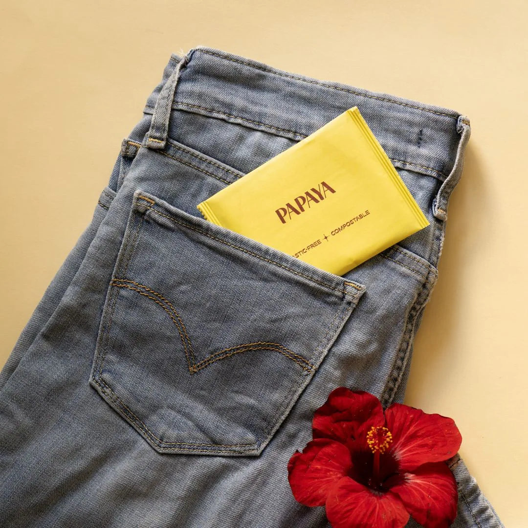 Blue jeans with a yellow 'PAPAYA' pouch and a red flower on a beige background